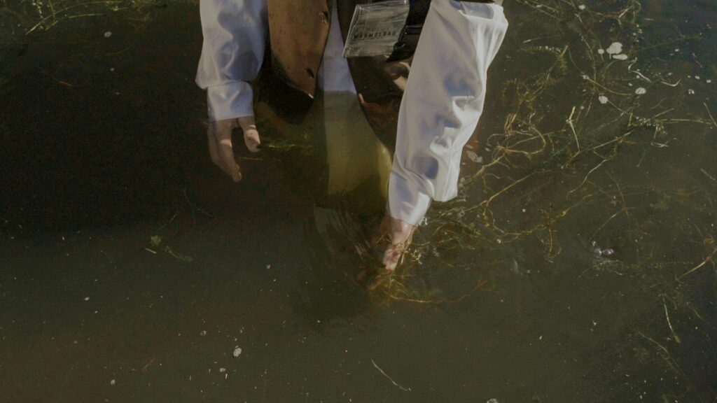 A person assessing water quality, standing in a lake with visible pollution.