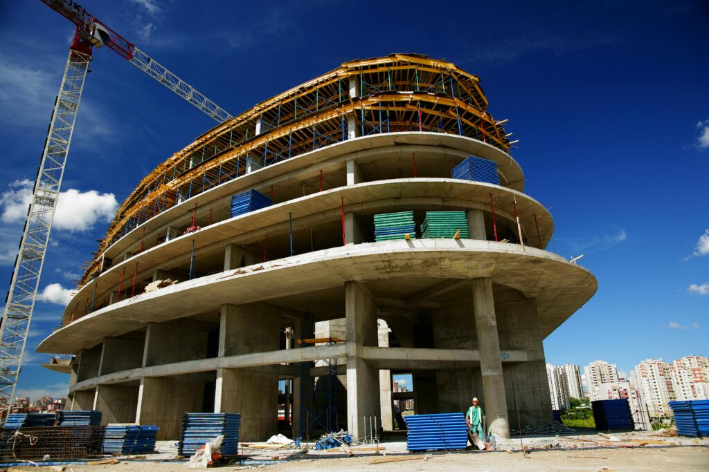 Low angle view of a circular building under construction with a crane, clear blue sky.