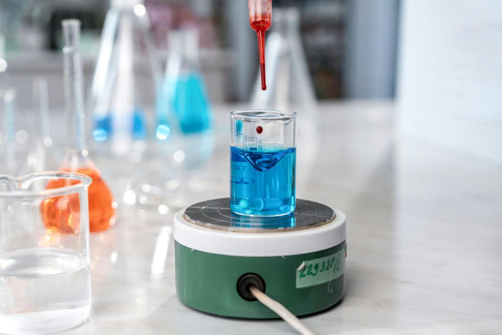 A laboratory experiment with a dropper adding red liquid to blue solution in glassware on a magnetic stirrer.