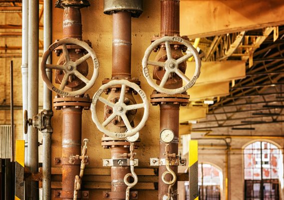 Close-up of rusty industrial pipes and valves, showcasing aging machinery in a factory setting.